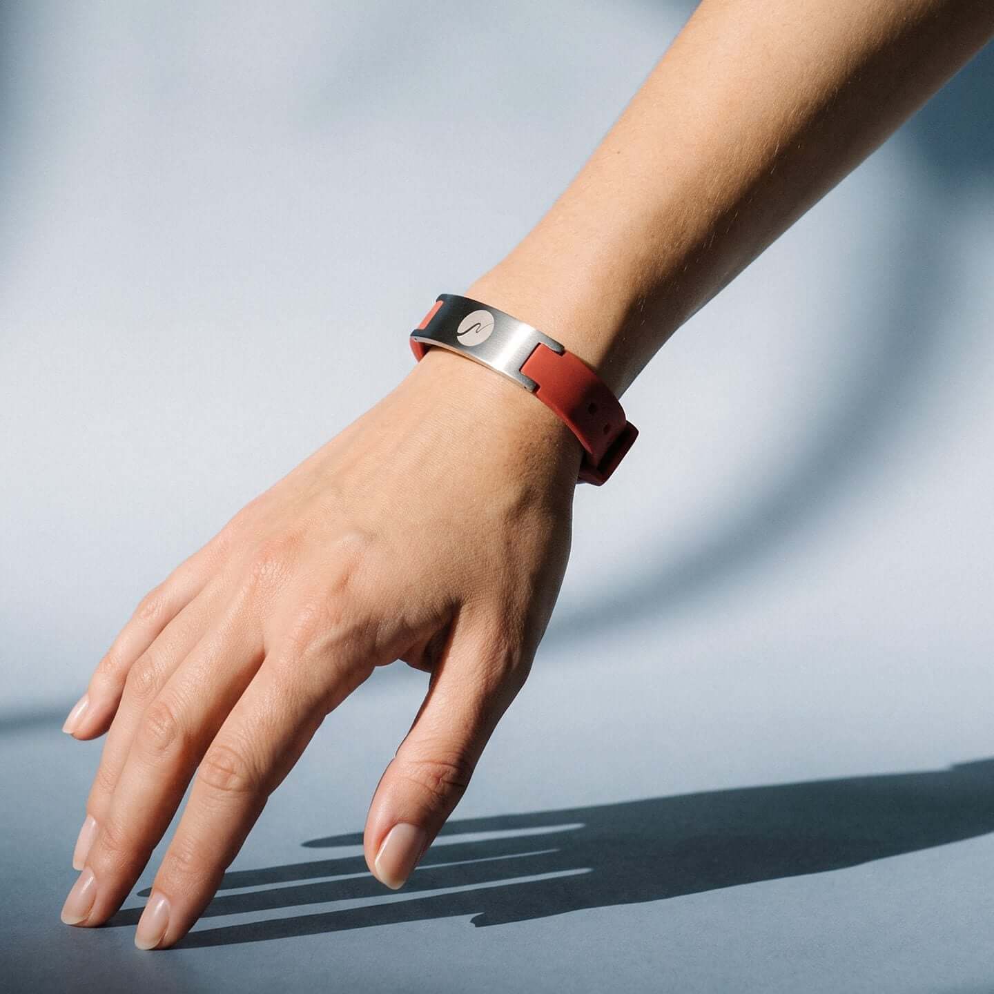 neowake Energy Bracelet in Silber und Rot am Handgelenk, Hand berührt eine helle Fläche